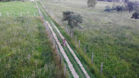 aerial panning shot of a young girl riding her bike down a country lane