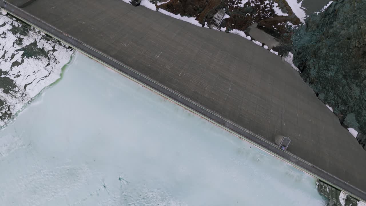 Frozen Cormor River In The Alpe Gera Dam, Gravity Dam During Winter In Valmalenco, Italy. - aerial shot