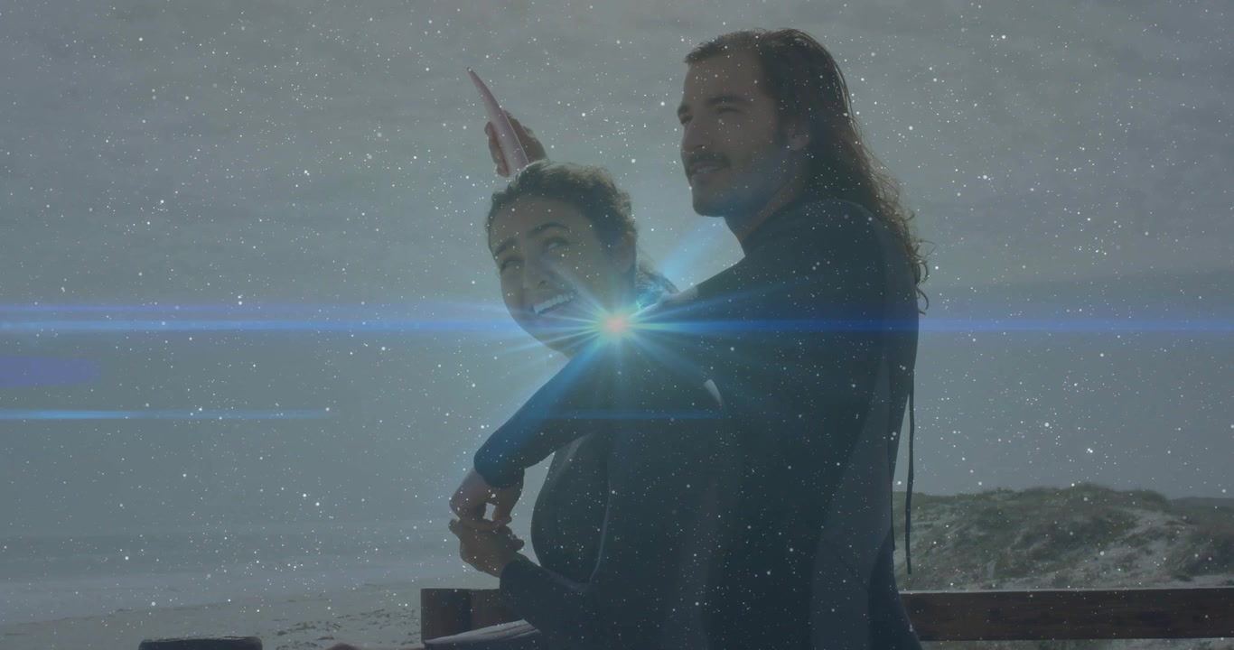 Luz solar causando reflexo na lente, homem abraçando mulher de frente para o oceano perto de uma prancha de surfe, compartilhando um momento de viagem