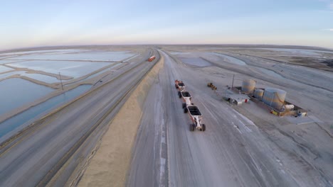 Toma-Aerea-De-Un-Gran-Camion-Vacio-Pasando-Frente-A-Otro-Lleno-De-Sal-En-Guerrero-Negro,-Laguna-Ojo-De-Liebre,-Reserva-De-Biosfera-De-El-Vizcaino,-Baja-California-Sur