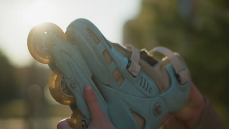 a close-up shot of a light blue rollerblade being held by a hand in a sunlit park. the sunlight filters through the background, creating a warm atmosphere, with the rollerblade prominently displayed