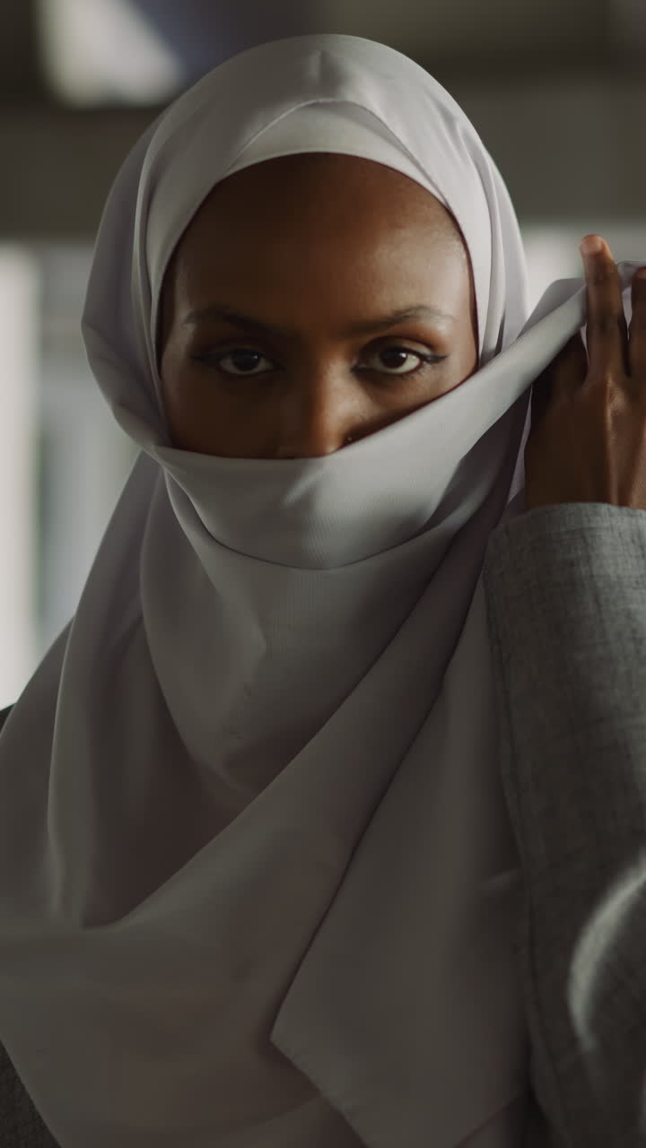 Elegant African-American woman raises up edge of hijab to hide face on embankment slow motion. Pretty Muslim lady in old town. Islamic lifestyle