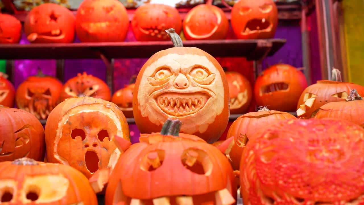 A terrifying and scary carved pumpkin sits outdoors on a shelf of of market stall in daylight on Halloween, spooky, festive charm, surrounded with lots of pumpkins