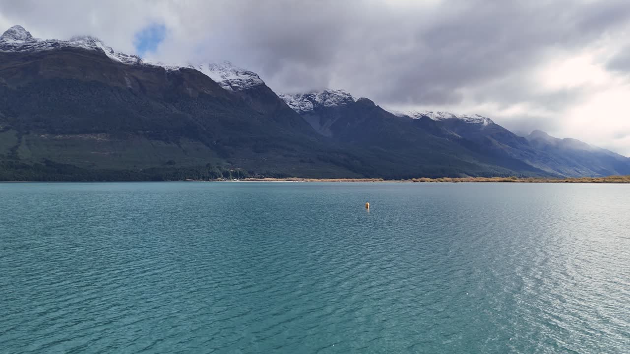 Tranquil lake with mountain backdrop under cloudy skies in Glenorchy, New Zealand. Calm waters and soft lighting create a peaceful atmosphere