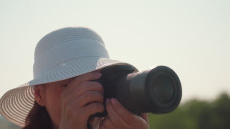 close up of woman in white top and sun hat adjusting camera to capture expansive country view under warm sunlight, soft breeze moving hair, serene smile reflecting joy of outdoor photography