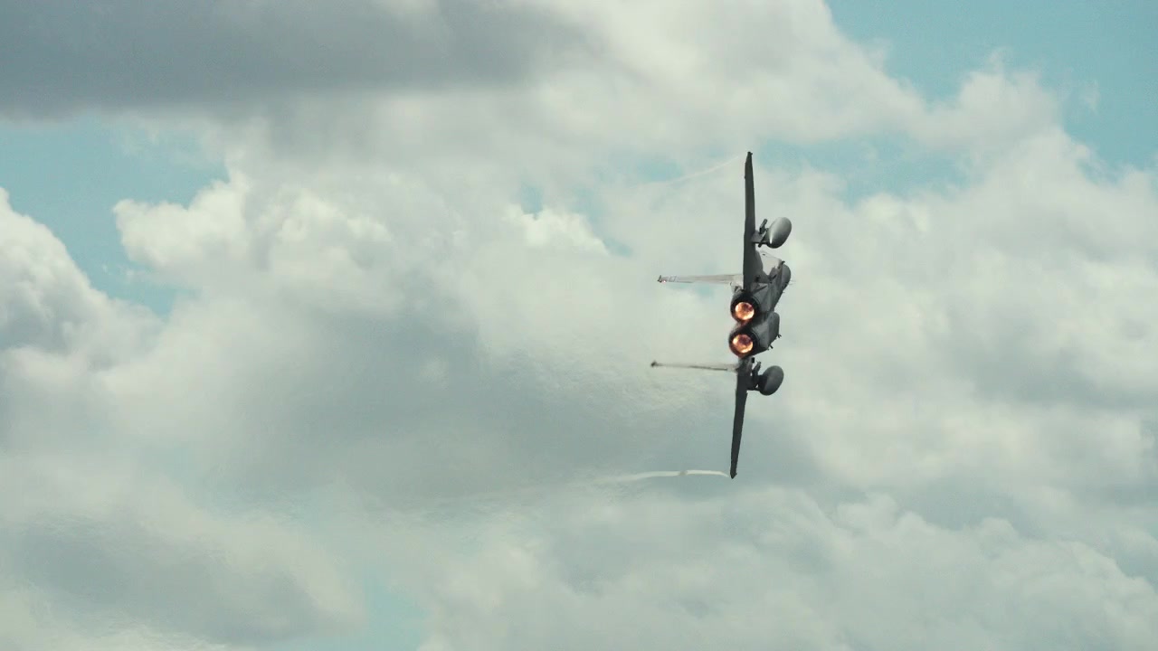 Un jet da combattimento militare esegue una virata inclinata ripida verso cieli nuvolosi