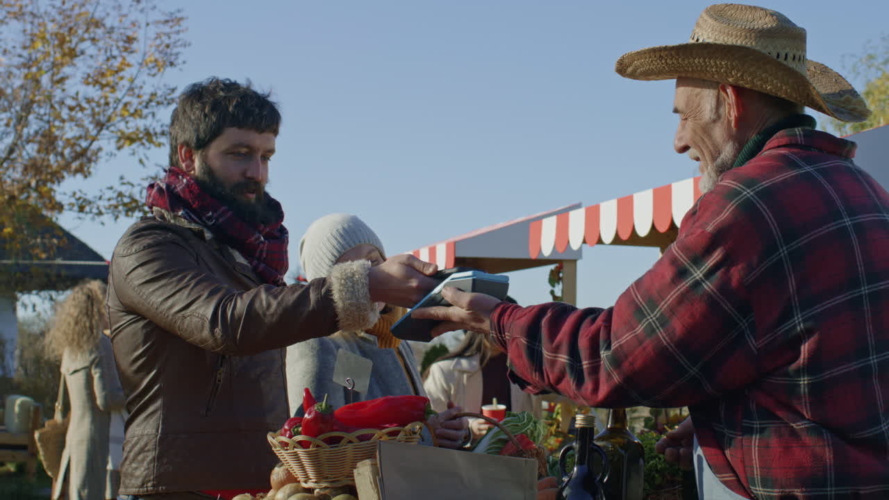 Spouses Shopping on Local Farmers Market Spouses Shopping on Local Farmers Market Wife Stands with Basket of Fruits or Vegetables Husband Pays for Purchase by Contactless Way Vegetarian and Organic Food Agriculture Closeup View