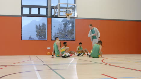 multiracial group of male basketball players with coach in gym, huddling and listening to coach