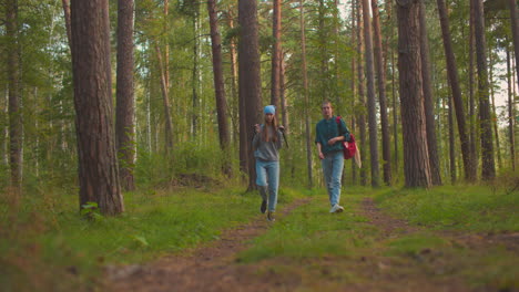 friends walk along a scenic forest trail surrounded by lush greenery, one playfully swings her black bag over her shoulder, while the other stays focused