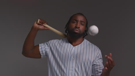 studio portrait of serious male baseball player wearing team shirt holding bat out towards camera shot against grey background 1