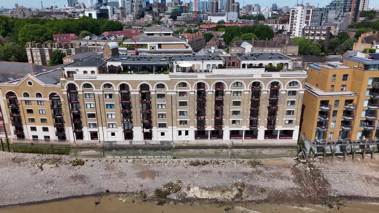 Przekształcone apartamenty w magazynach nad rzeką z wysokimi łukowymi oknami stoją nad brzegiem, obok nowoczesnych bloków z cegły