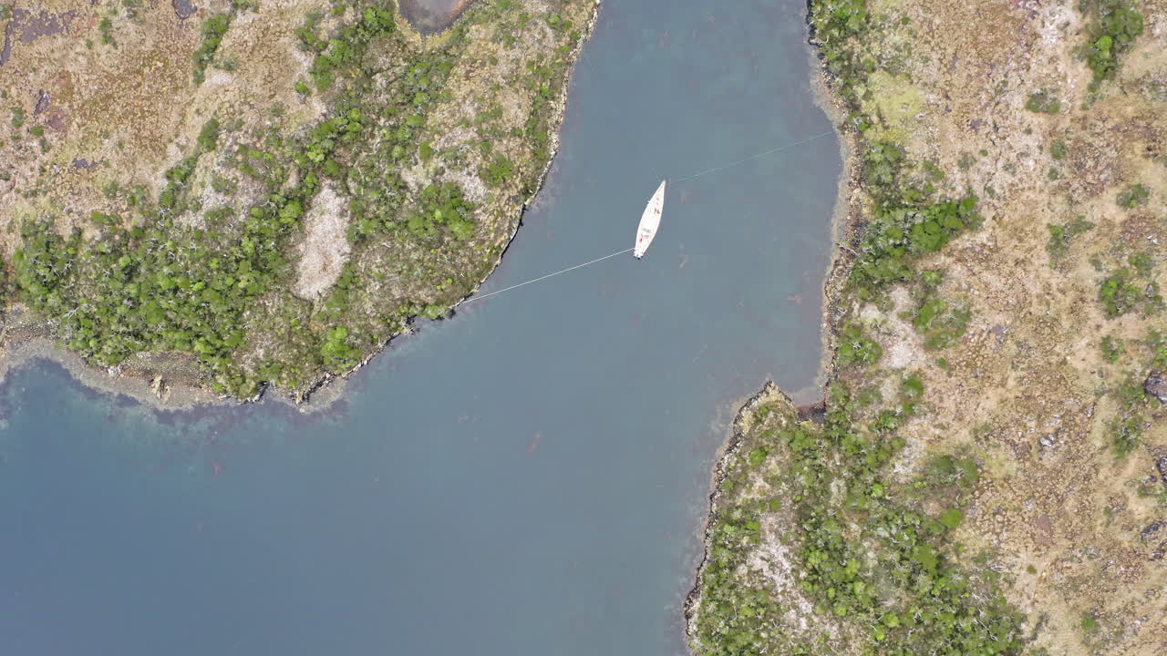 Aerial top-down overview of narrow channel between forested islands in Beagle Channel with boat anchored tied down in water