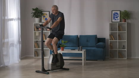 sporty man is training on stationary bike in home cardio workout for keeping good physical condition in middle age fitness and sport