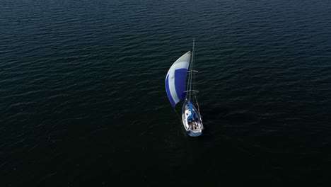 Aerial-perspective-of-a-sailboat-sailing-with-its-vibrant-sail,-gliding-on-the-dark-waters-of-the-Baltic-Sea