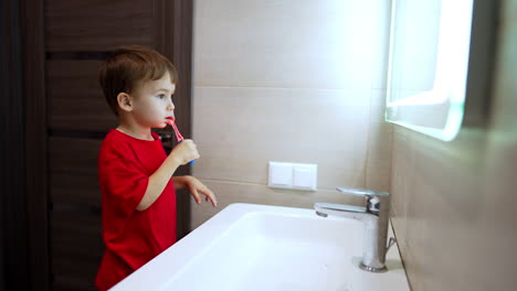 cheerful caucasian toddler brushing teeth in the bathroom. lovely baby completing his personal hygiene at home.