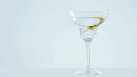 Animation-of-red-specks-moving-over-cocktail-glass-with-olives-on-white-background