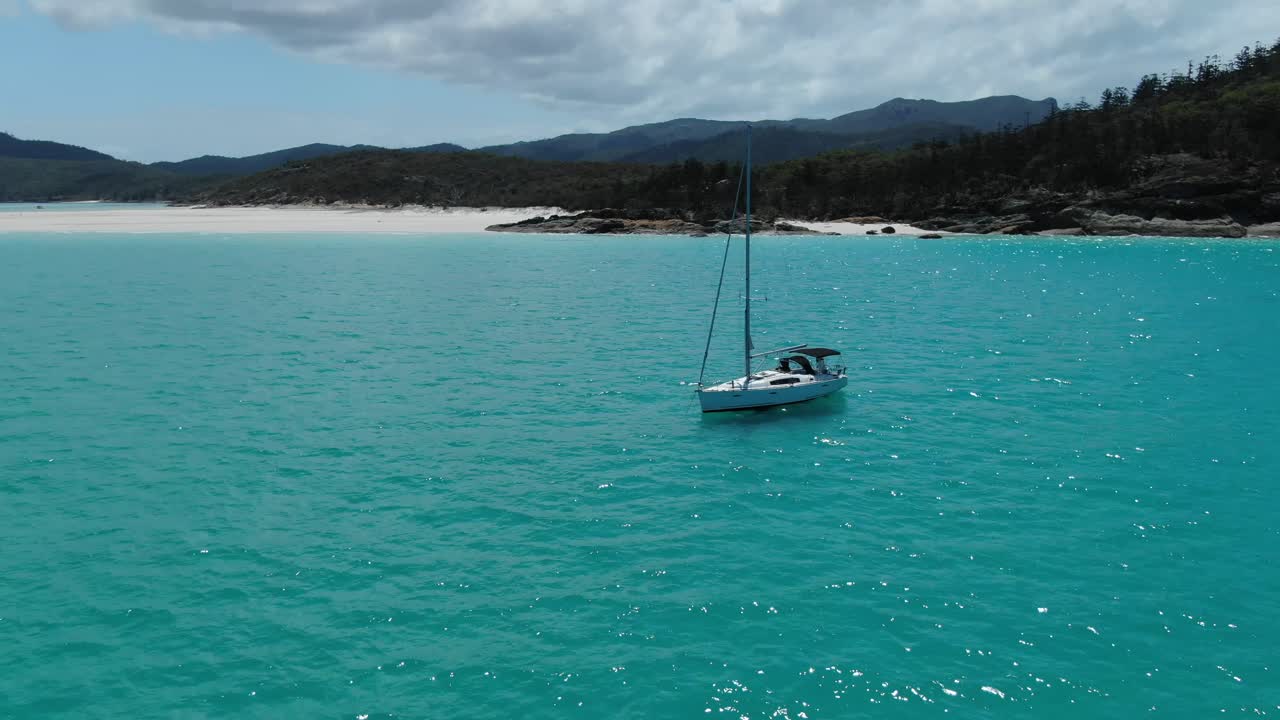 un velero blanco se encuentra en las aguas turquesas del océano frente a la costa de la playa white haven, whitsundays, australia