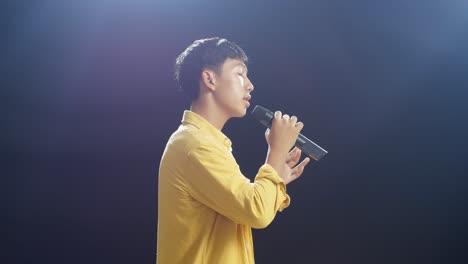 side view of young asian boy holding a microphone and singing on the black background