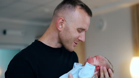 happy caucasian dad kissing his newborn's nose and fingers. loving dad taking care of his child. close up. blurred backdrop.