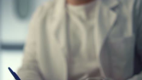 man surgeon writing notes in medical journal sitting hospital office close up.