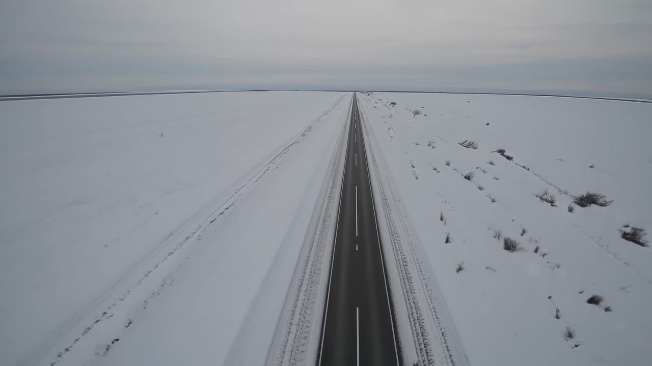 Aerial video captures a straight road cutting through a vast, snow-covered landscape