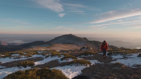 Young-hiker-with-red-down-jacket-and-backpack-walkig-towards-the-camera