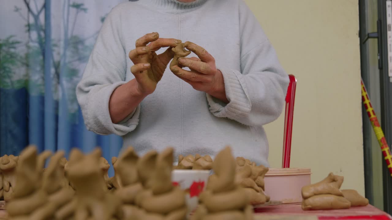 한 아시아 여성이 기념품 플루트를 위해 찰흙으로 동물 형상을 만들고 탄 하의 관광과 전통 공예품을 정면에서 보여줍니다.