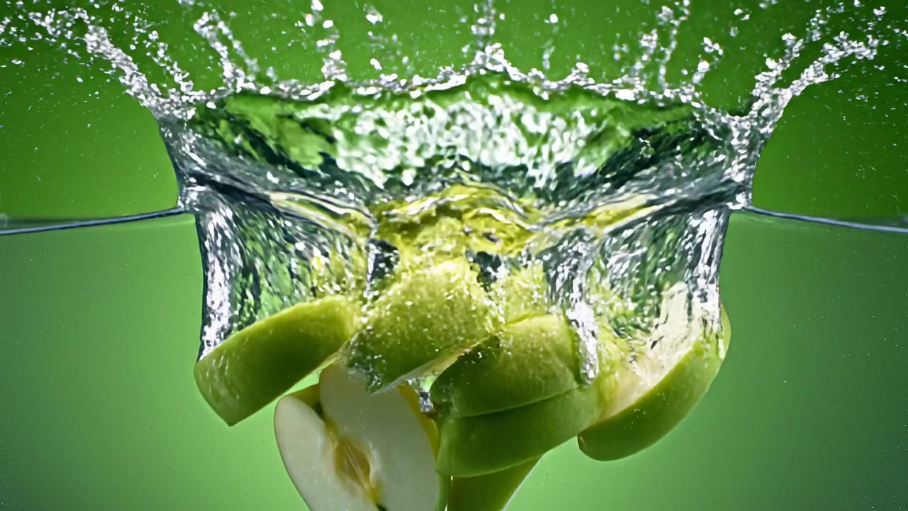 Green apple slices falling into water on green background