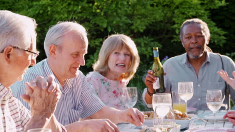 group of senior friends enjoying outdoor dinner party at home