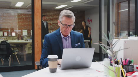 businessman and businesswoman working on computers in open plan office with colleagues in background