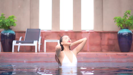 Sexy-Sensual-Woman-Smooth-Wet-Hair-with-Hands-Inside-Exotic-Swimming-Pool-in-Bali,-Indonesia,-slow-motion-portrait-front-view