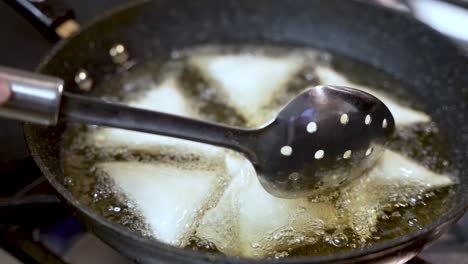 metal slotted spoon stirring samosas in hot oil in a pan, during their preparation in an indian restaurant kitchen