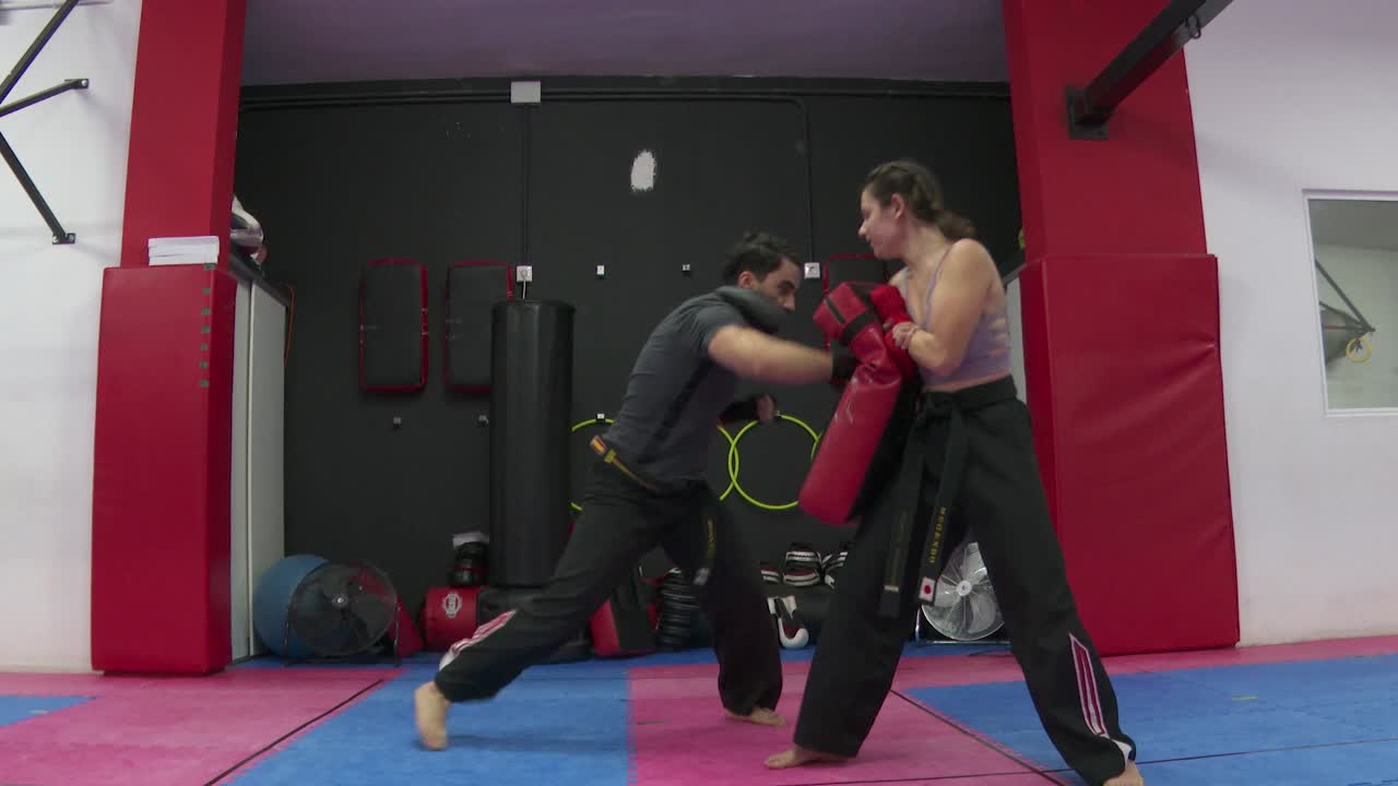 Strong Man trains boxing and kicks on a training device that a woman is holding