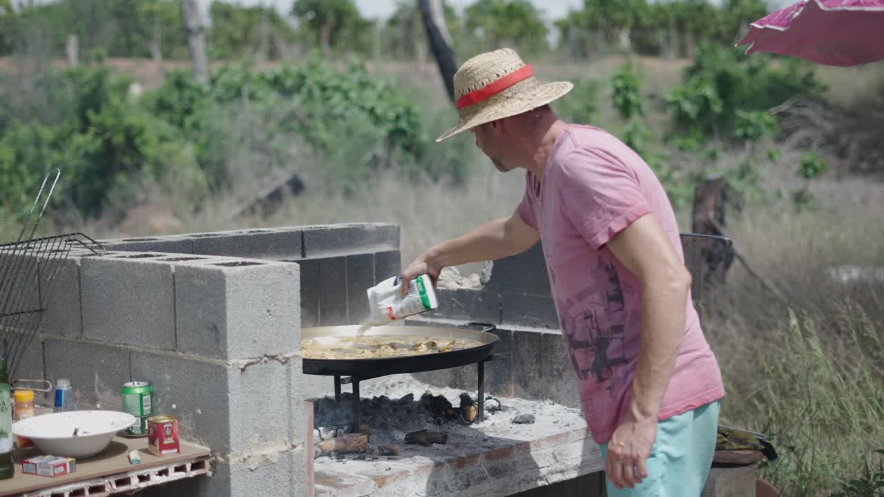 Man cooking paella outdoors over an open fire barbecue