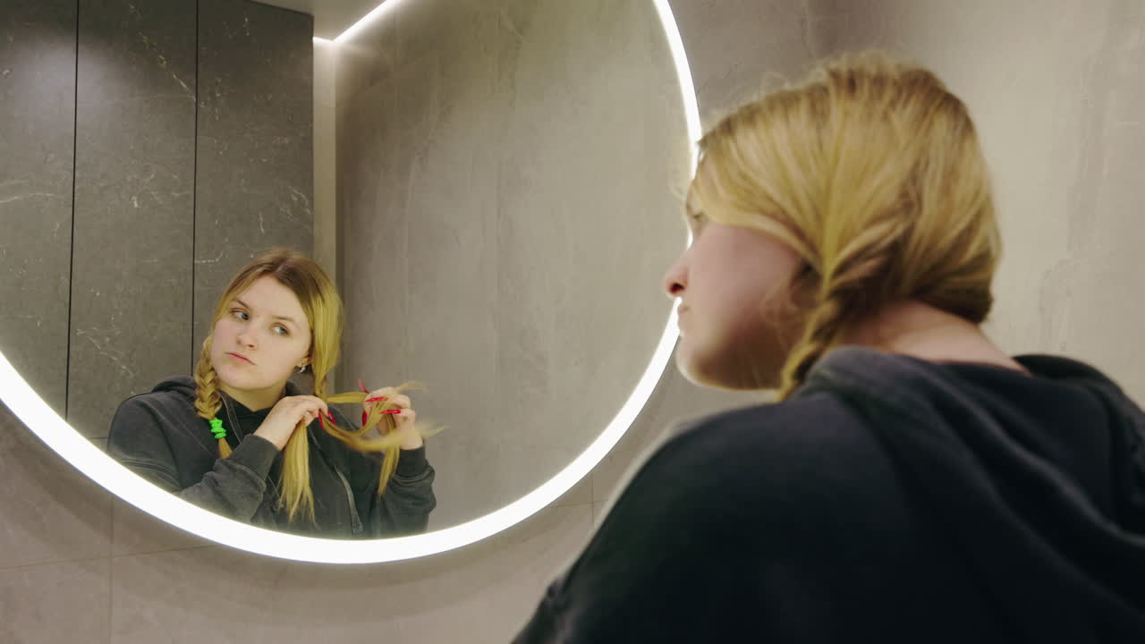 Woman Styling Her Hair in Bathroom Mirror