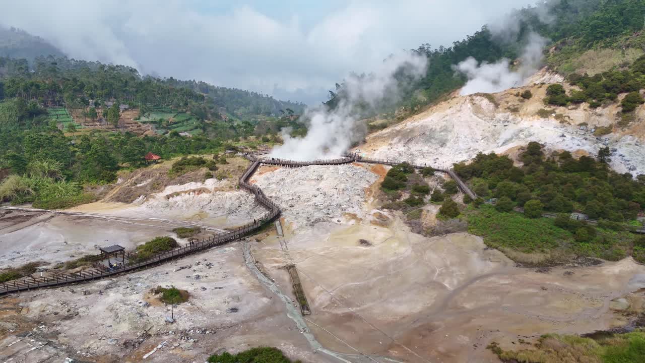Drone flying over volcanic activity at Sikidang Crater, a famous geothermal site in the Dieng Highlands, surrounded by lush greenery and hills