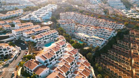 Experience-an-enchanting-aerial-circle-flight-on-a-sunny-day-over-a-vibrant-residential-area-in-Tenerife,-Spain,-boasting-a-stunning-array-of-hundreds-of-condos-and-picturesque-coastal-views