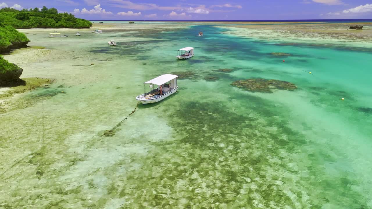 Stunning aerial view of tour boats in the crystal-clear, shallow turquoise waters of a tropical lagoon, revealing the vibrant coral reef and sandbars below