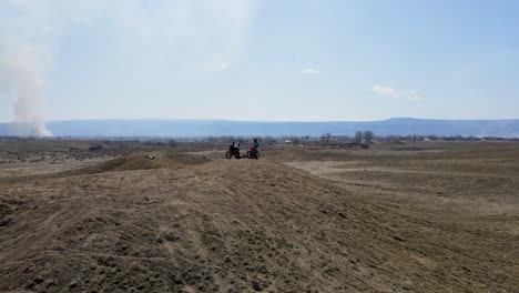 A-spectacular,-fast-paced-drone-shot-of-two-motocross-riders-preparing-to-hit-a-big-hill-jump,-in-the-desert-like-terrain-of-Grand-Valley-OHV-area,-located-in-Grand-Junction,-Colorado