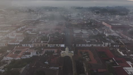 Tilt-up-shot-of-Santa-Catalina-arch-at-Antigua-foggy-sunrise,-aerial