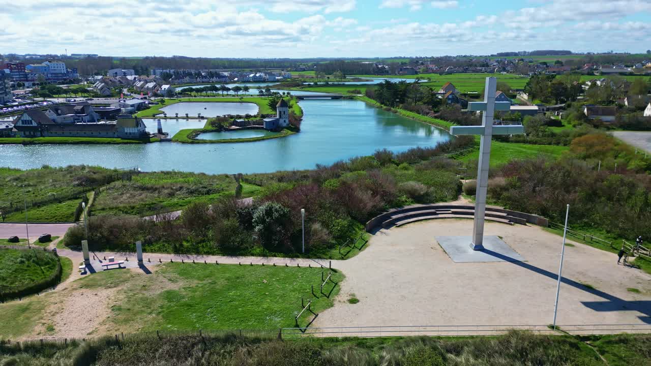 Croix de Lorraine monument with windmill on l'ile de Benoist in background, Courseulles-sur-Mer, Normandy, France. Aerial drone sideways