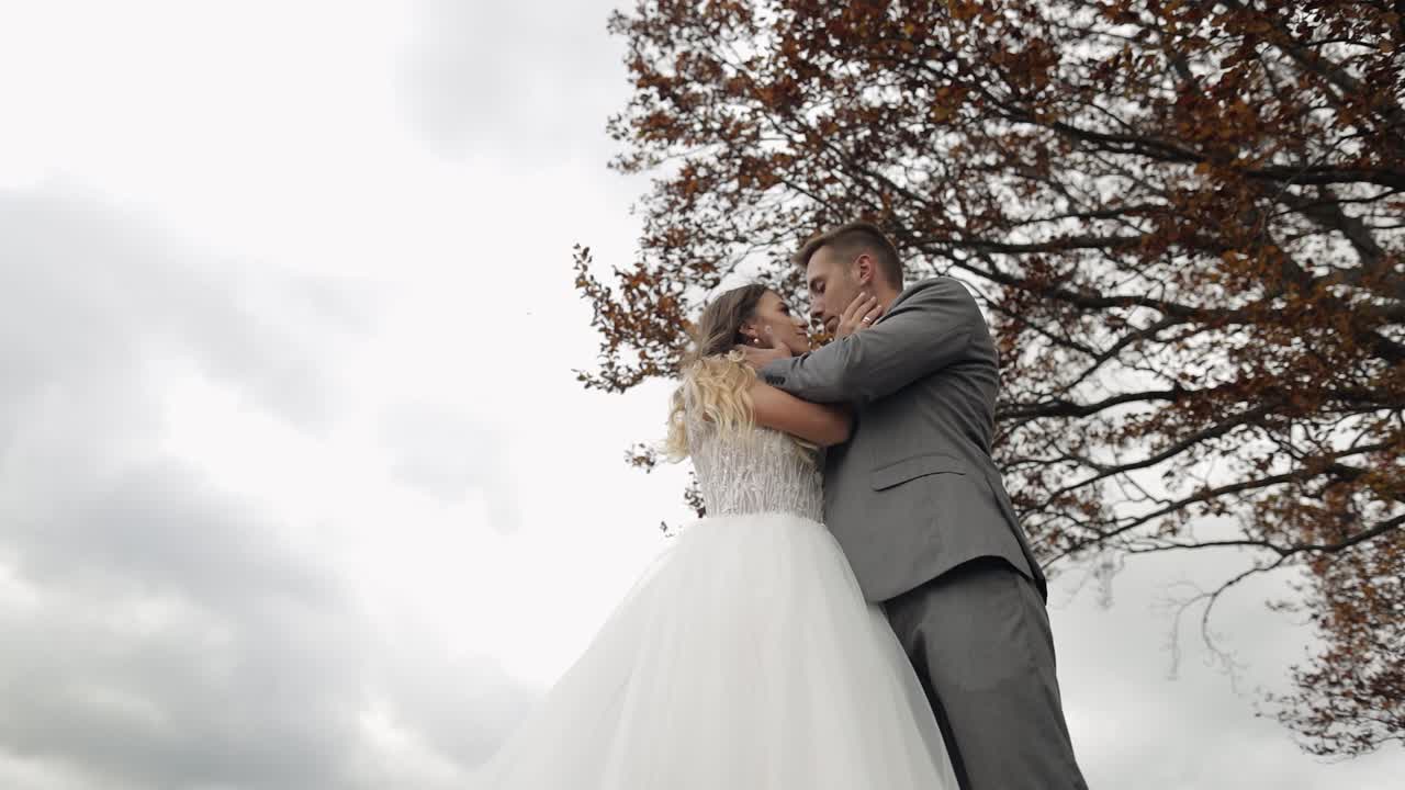 Lovely young newlyweds bride groom embracing on cloudy sky background, wedding couple family in love