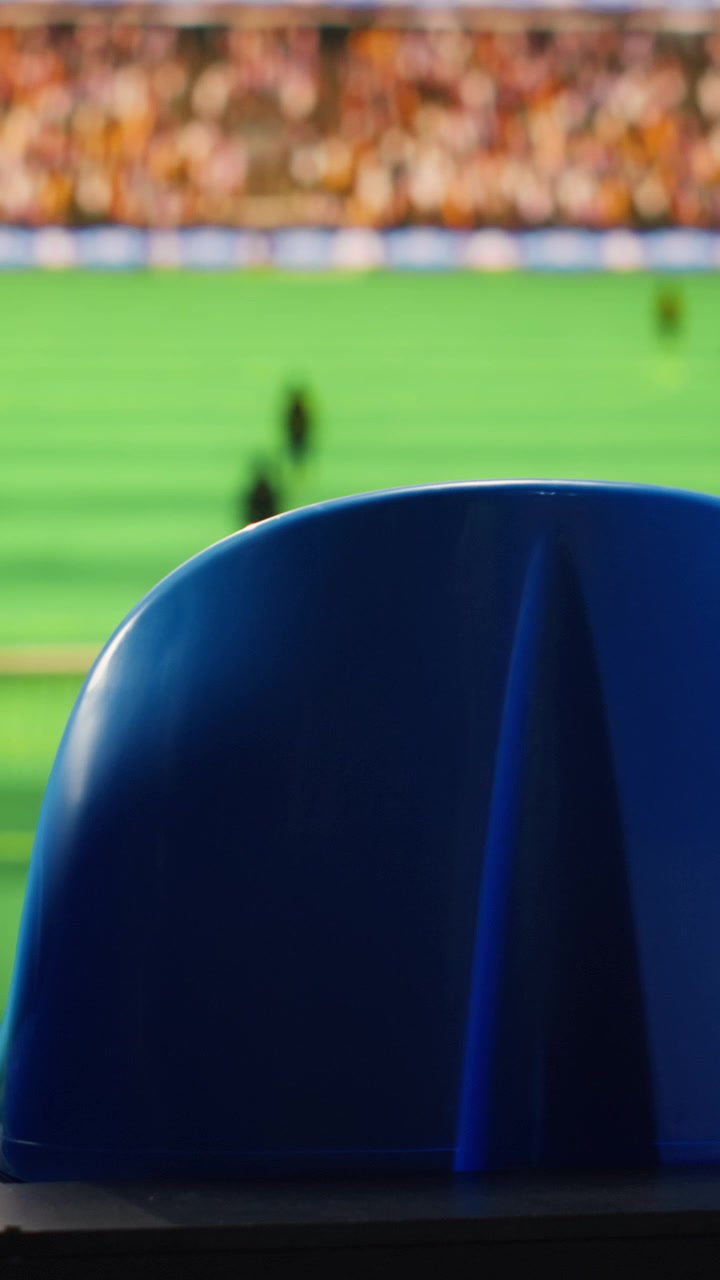 Video verticale. Primo piano di sedili blu dello stadio e campo da calcio sfocato con giocatori.