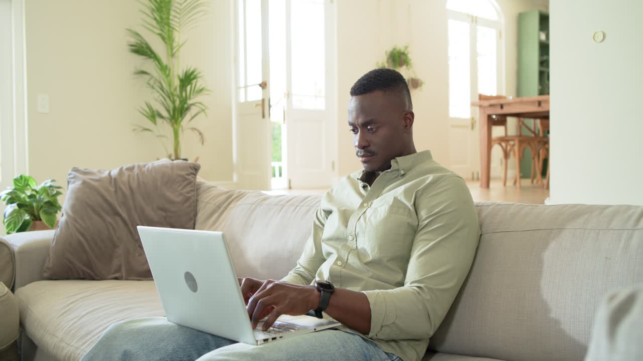 African American man on sofa typing, ending work, closing laptop, grabbing headset, rubbing hands