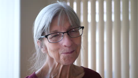 A-happy-old-caucasian-woman-with-aging-face-wrinkles-gray-hair-and-glasses-looking-at-camera-and-smiling-with-a-shy,-positive-and-optimistic-outlook-on-life