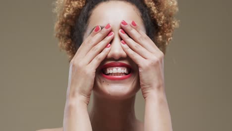 Happy-biracial-woman-with-dark-hair-and-red-lips-and-nails-on-beige-background,-slow-motion