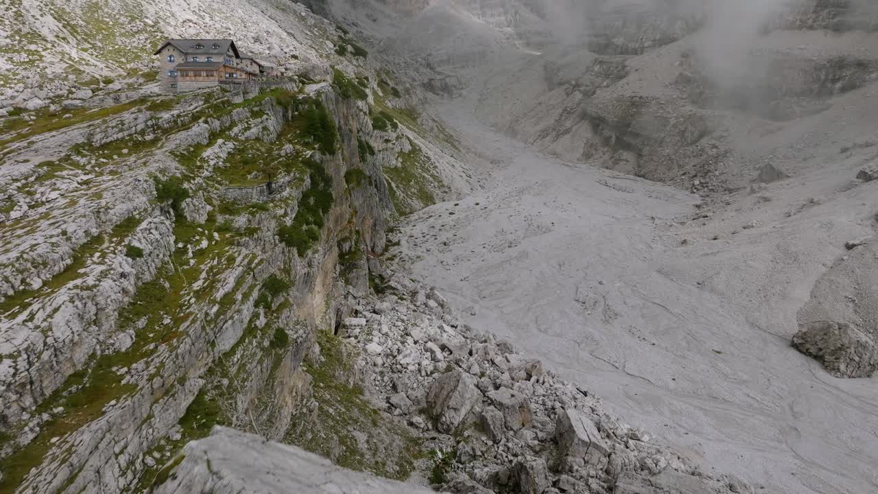 toma aérea inclinada hacia arriba del gigantesco paisaje montañoso con valle rocoso y cabaña para excursionistas - brenta dolomitas en italia