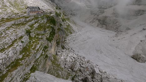 Toma-Aérea-Inclinada-Hacia-Arriba-Del-Gigantesco-Paisaje-Montañoso-Con-Valle-Rocoso-Y-Cabaña-Para-Excursionistas---Brenta-Dolomitas-En-Italia