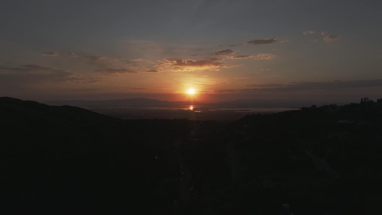 Aerial drone time-lapse shot from Bountiful Canyon in Utah at golden hour with road, forest, valley homes, Wasatch Mountains, cityscape, and the Great Salt Lake at sunset
