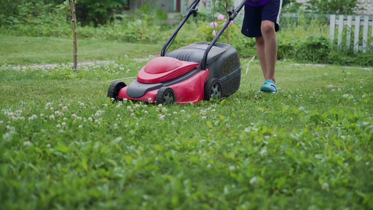 Young boy cutting the grass with a lawn mower in summer time. Outdoor seasonal household works